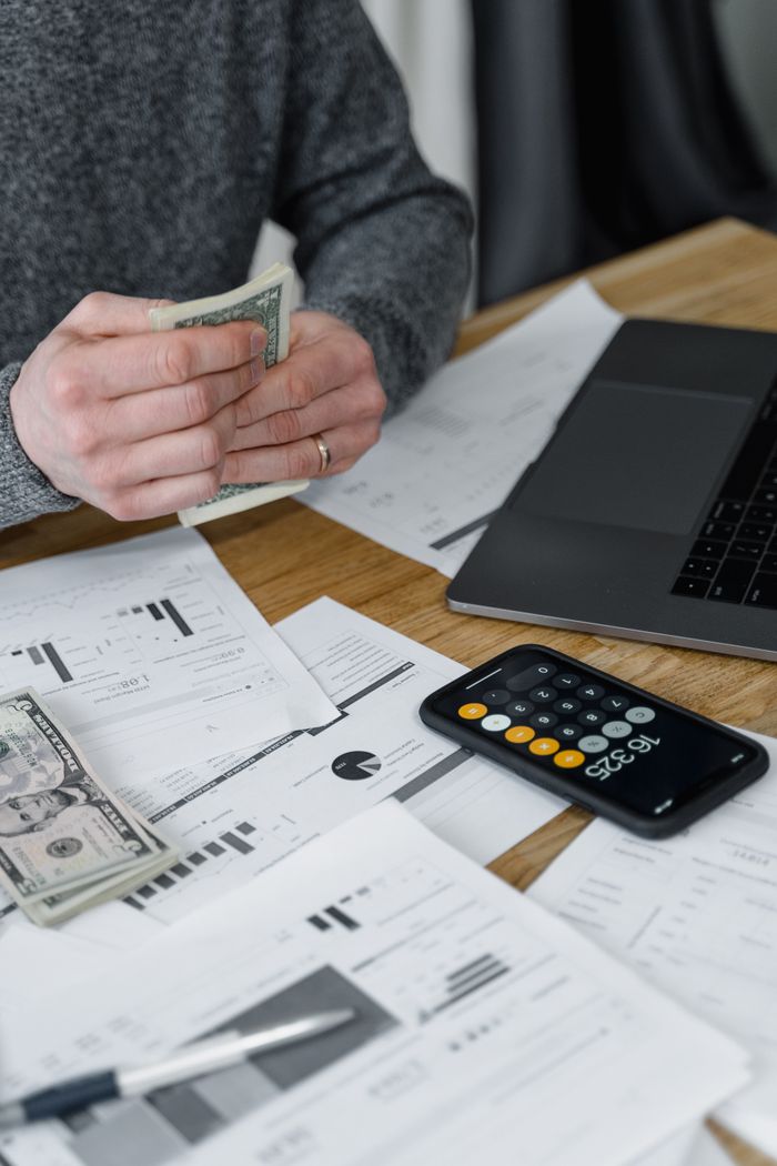 Crafting Captivating Headlines: Your awesome post title goes here Hands counting money at a workspace with a laptop, calculator, and financial documents.