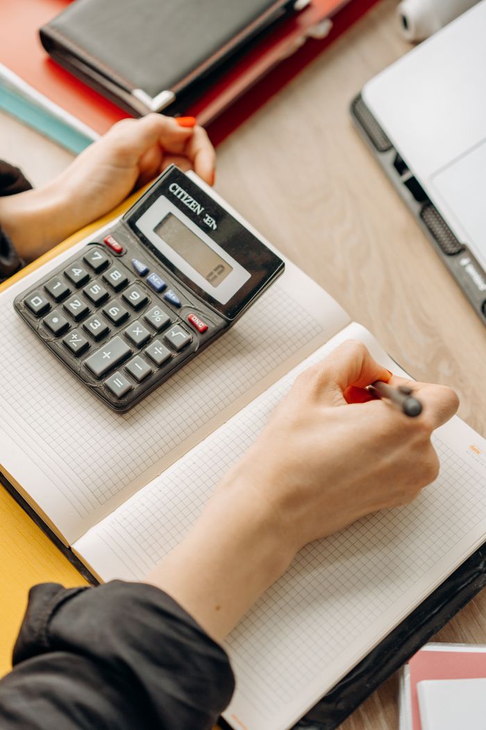 Mastering the First Impression: Your intriguing post title goes here Person writing in notebook with calculator nearby on a desk. Ideal for business or finance themes.